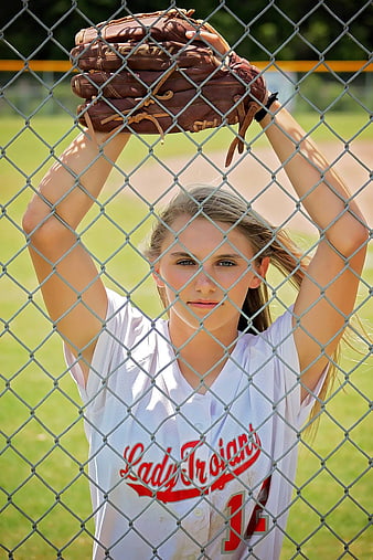 Female softball player holding mitt behind chain link fence