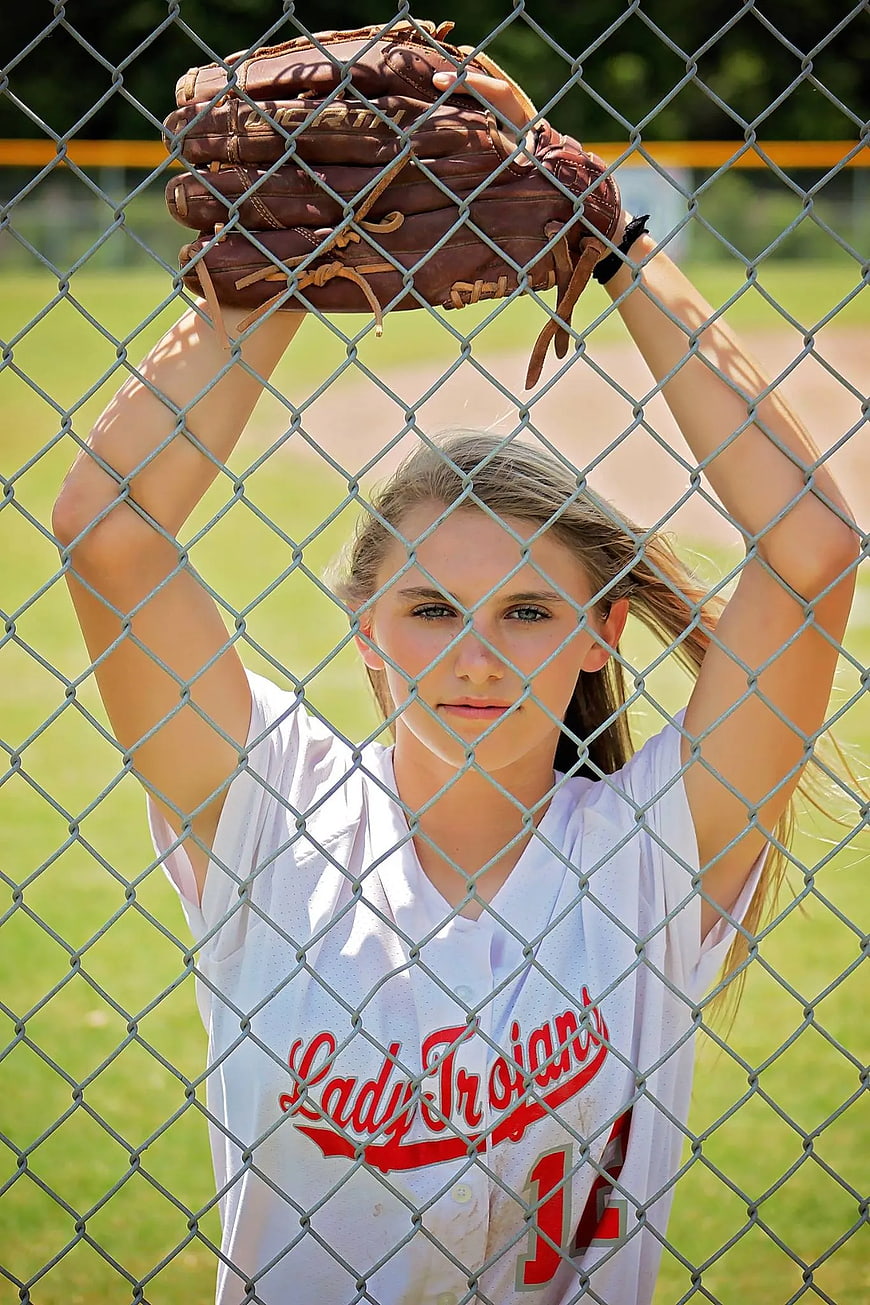 Female softball player holding mitt behind chain link fence
