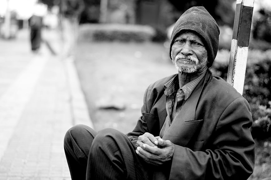 Black and white portrait of elderly man sitting on street