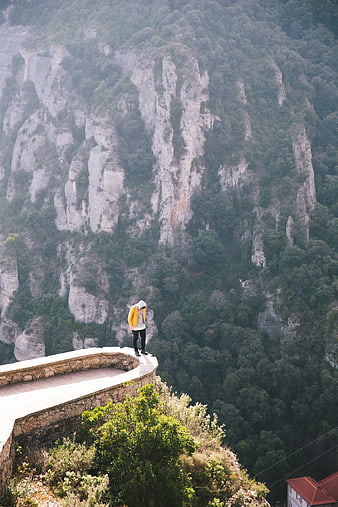 Man in Yellow Jacket Standing on Cliff Edge Overlooking Mountains