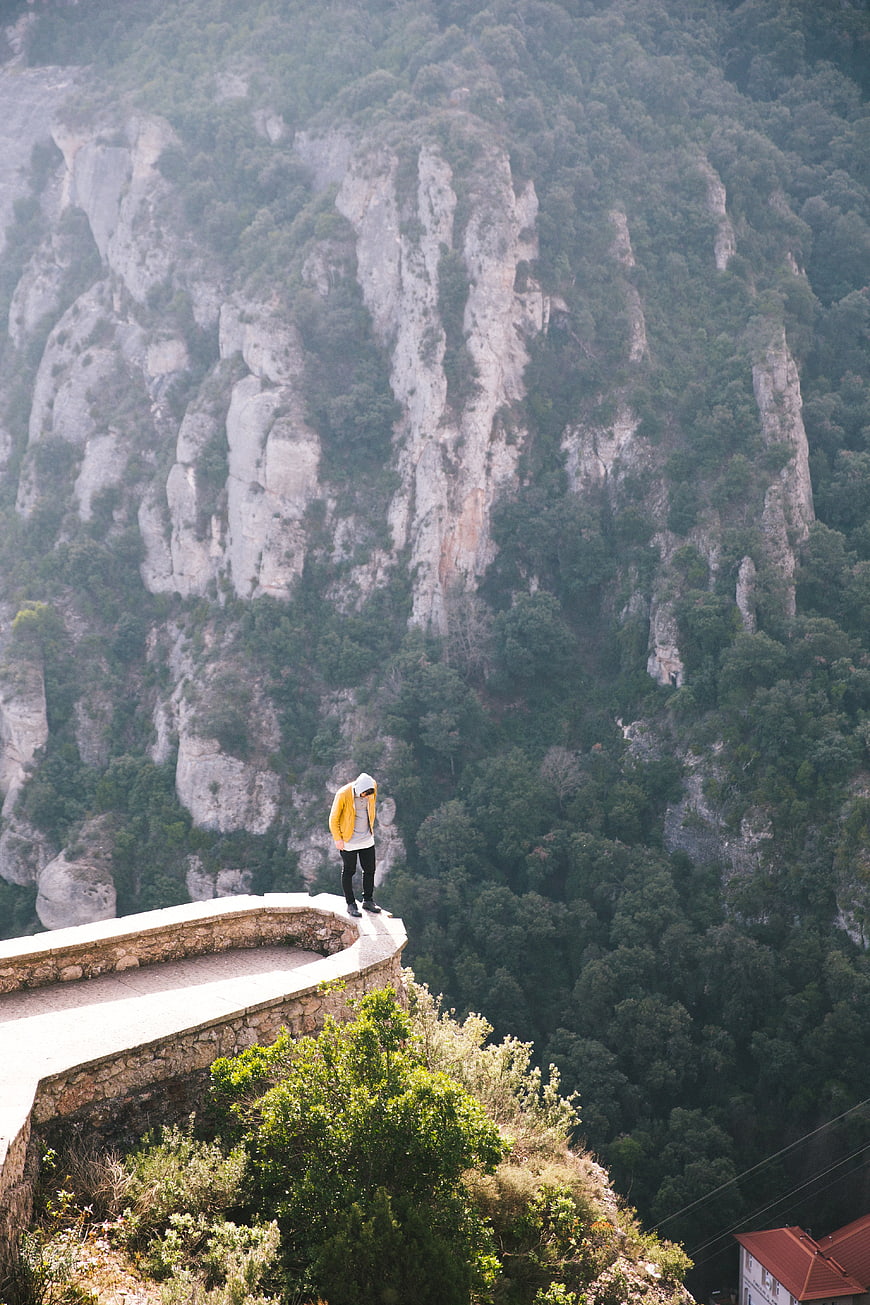 Man in Yellow Jacket Standing on Cliff Edge Overlooking Mountains