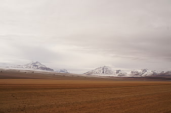 Vast Highland Landscape with Snow-Capped Mountains and Overcast Sky