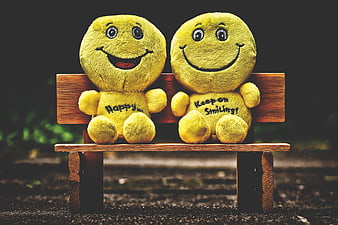 Two yellow smiley face plush toys sitting on a wooden bench