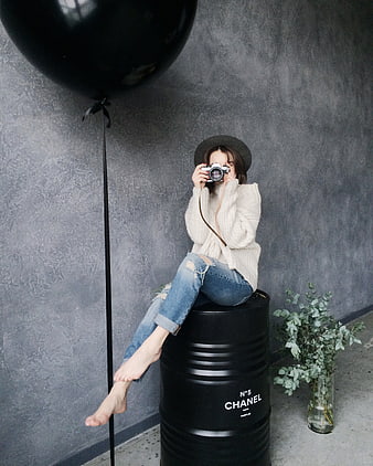 Woman Photographer Sitting on Black Barrel with Camera