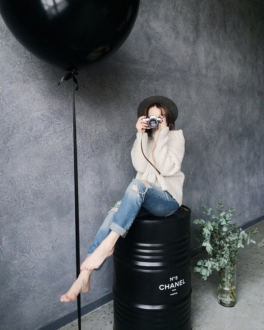 Woman Photographer Sitting on Black Barrel with Camera