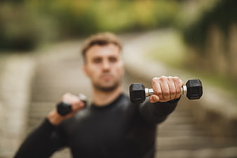 Man lifting dumbbells outdoors with shallow depth of field