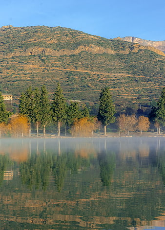 Serene lake with misty reflections and mountain backdrop