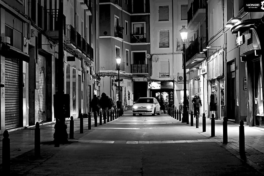 Black and White Night Street Scene with Car and Pedestrians