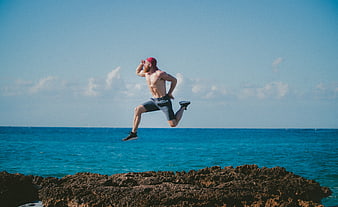 Shirtless Man Jumping on Rocks by Ocean