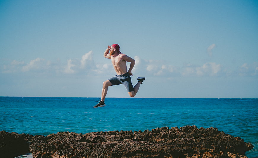 Shirtless Man Jumping on Rocks by Ocean