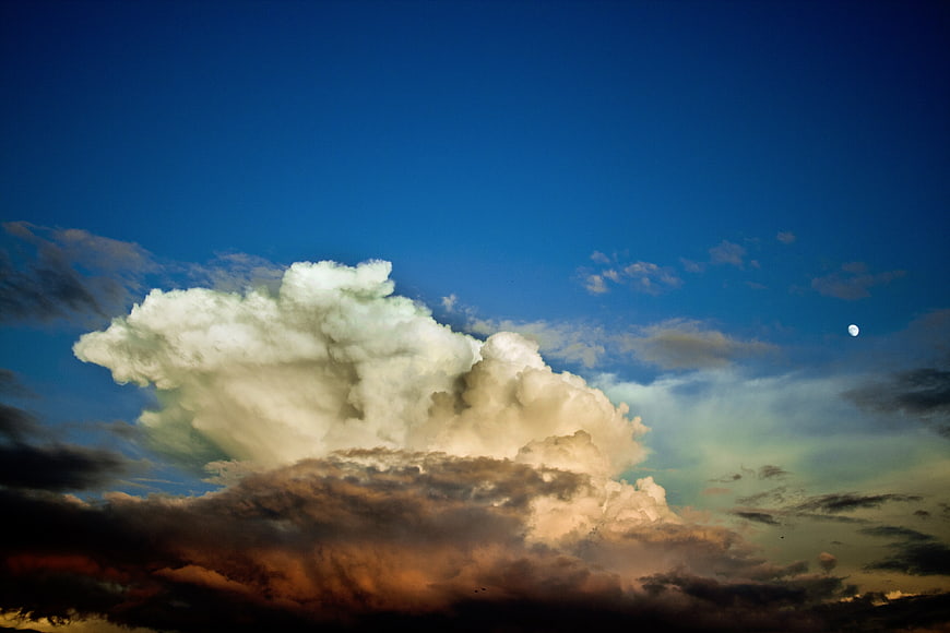 Dramatic cumulus cloud formation with moon in blue sky