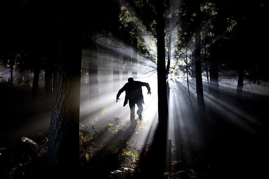 Silhouette of a man running through a misty forest with sunbeams