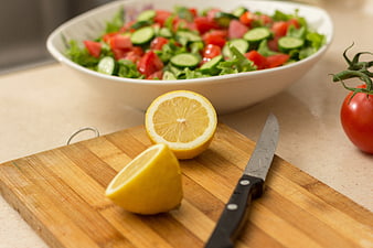 Fresh vegetable salad with lemon and knife on cutting board