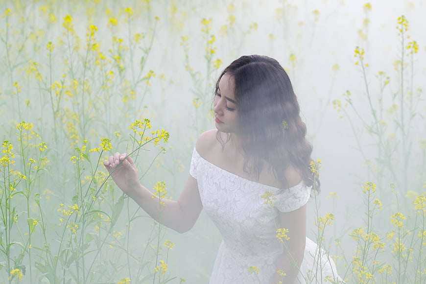Woman in white dress holding yellow flowers in misty field