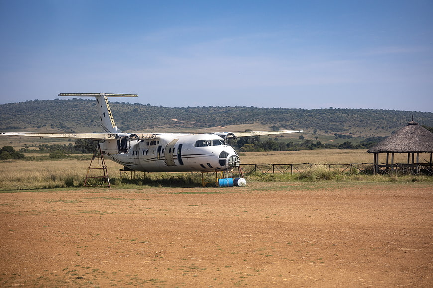 Abandoned white airplane on dry grassy field with hills