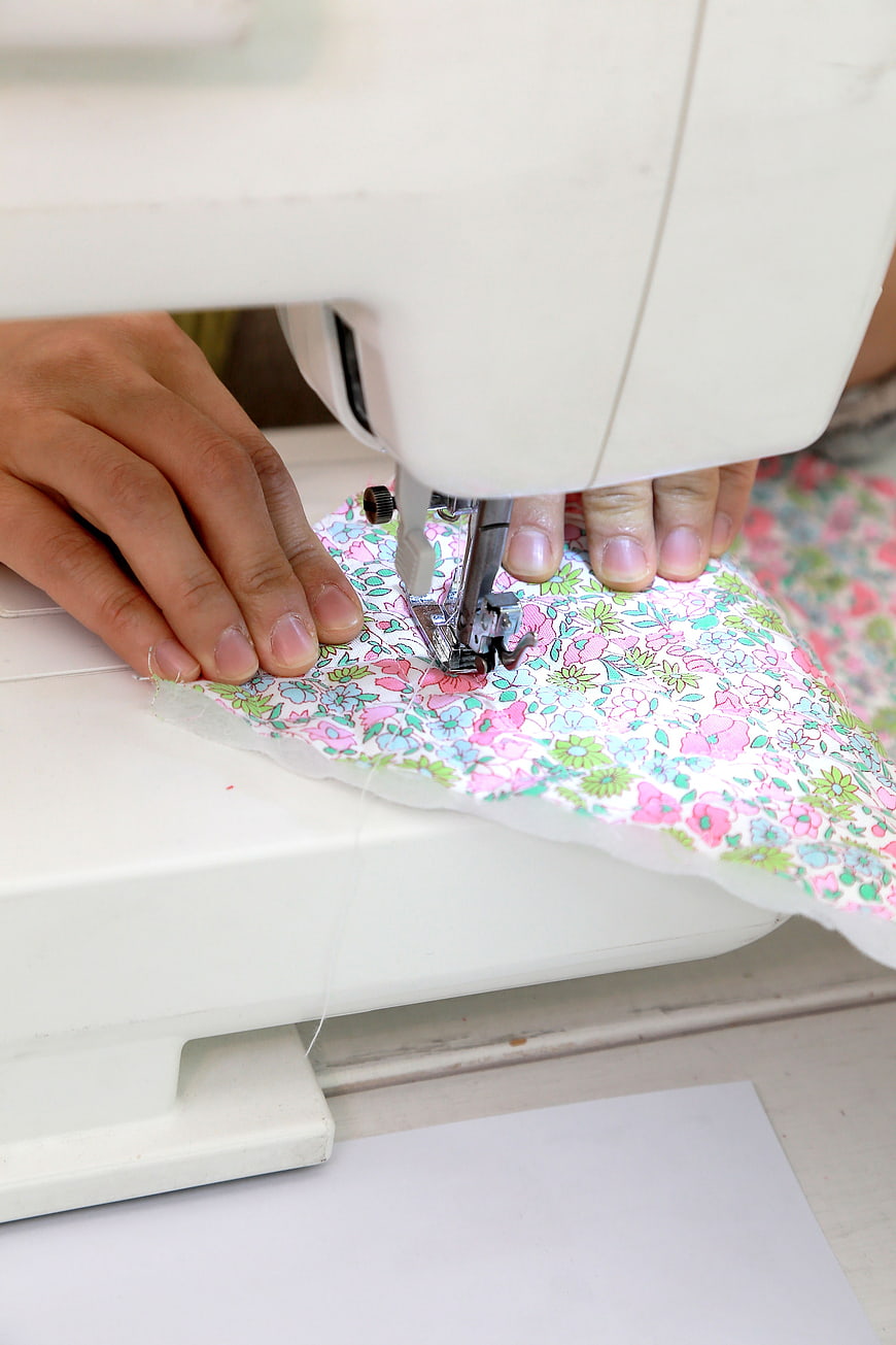 Hands Sewing Floral Fabric on White Machine