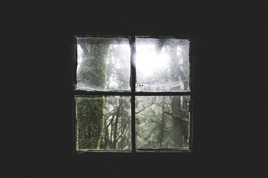 Old four-pane window looking out onto a misty forest