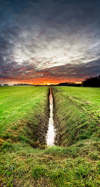 Dramatic sunset over green field with drainage ditch