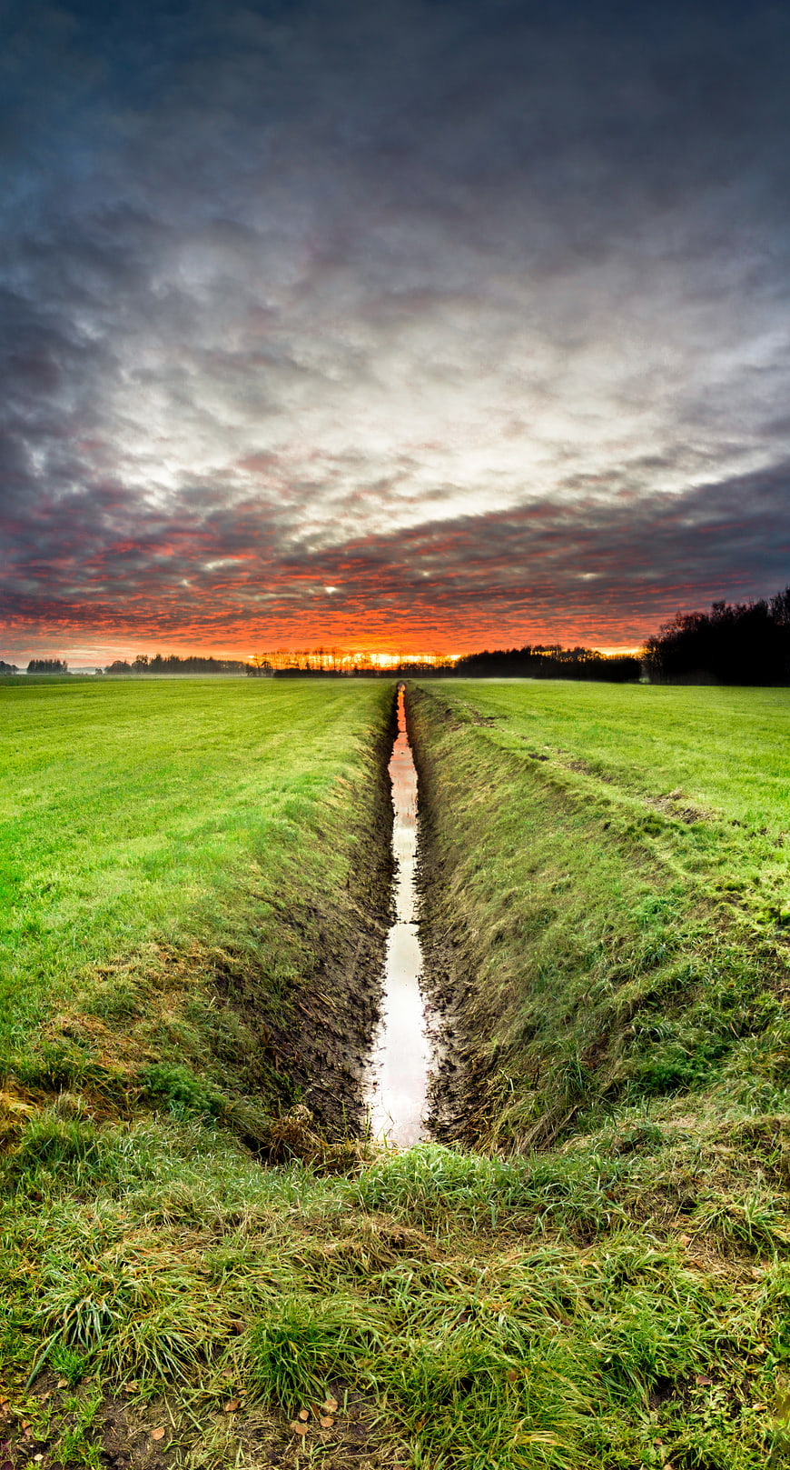 Dramatic sunset over green field with drainage ditch