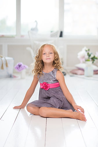 Young girl in sequined dress sitting on white wooden floor