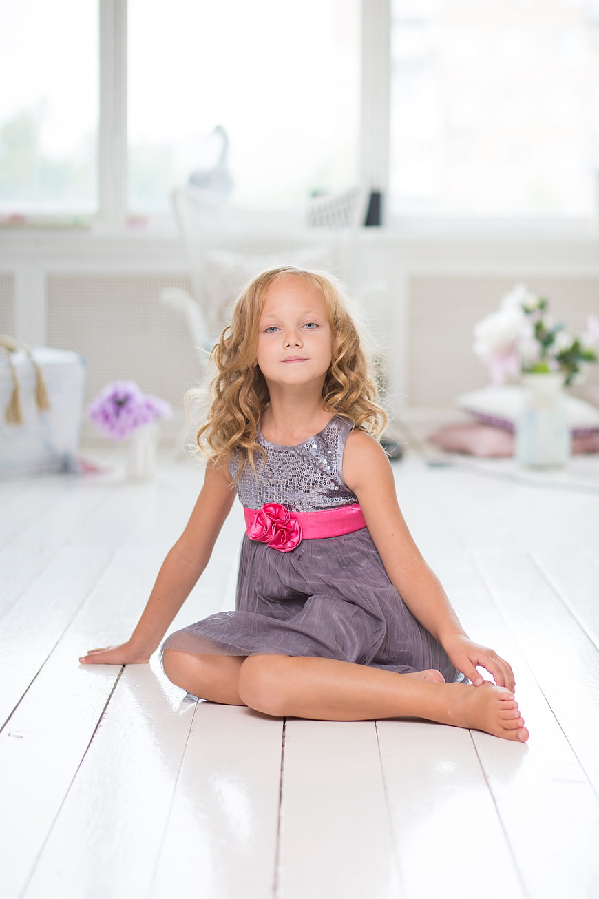Young girl in sequined dress sitting on white wooden floor