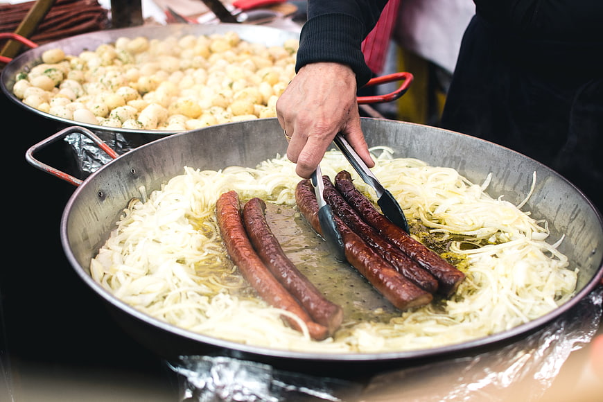 Cooking sausages and onions in large pan