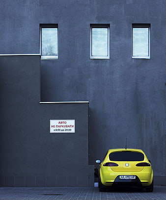 Yellow car parked illegally against gray modern building wall