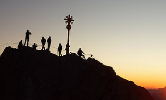Silhouettes of hikers at mountain summit cross at sunrise