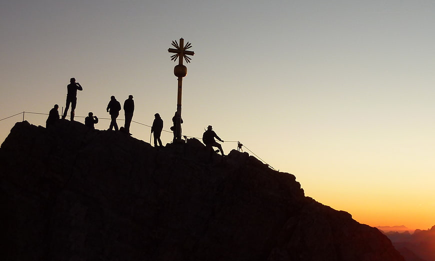 Silhouettes of hikers at mountain summit cross at sunrise