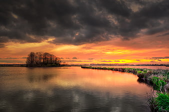 Dramatic sunset over river with dark storm clouds and vibrant orange sky