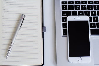 Flat lay of notebook, pen, smartphone, and laptop keyboard