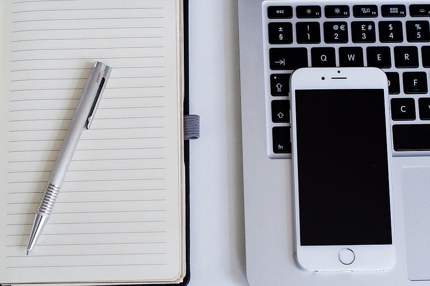 Flat lay of notebook, pen, smartphone, and laptop keyboard