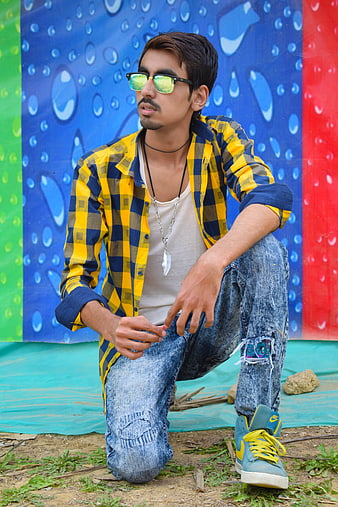 Stylish young man in plaid shirt kneeling against colorful mural