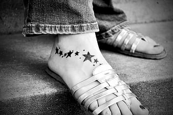 Black and white close-up of a star tattoo on a woman's ankle