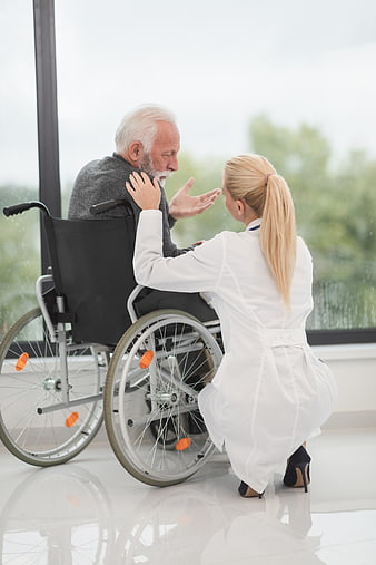Female doctor comforting elderly man in wheelchair