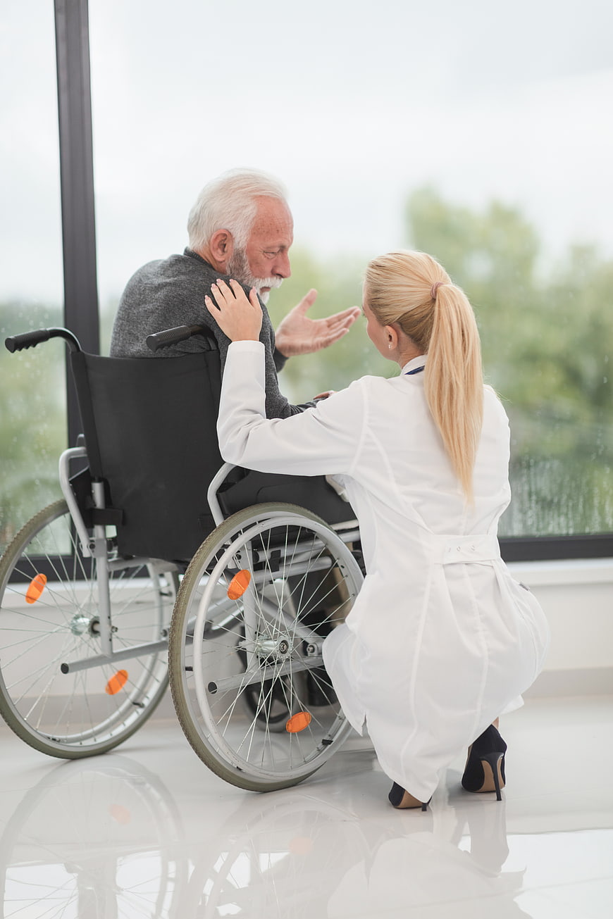 Female doctor comforting elderly man in wheelchair
