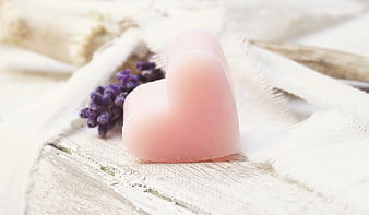 Pink heart-shaped soap with lavender sprig on rustic white wooden surface