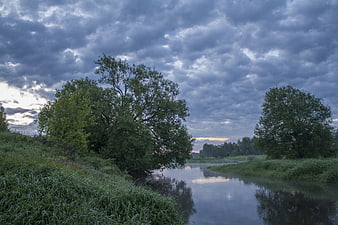 Dramatic cloudy sky over a calm river with lush green trees