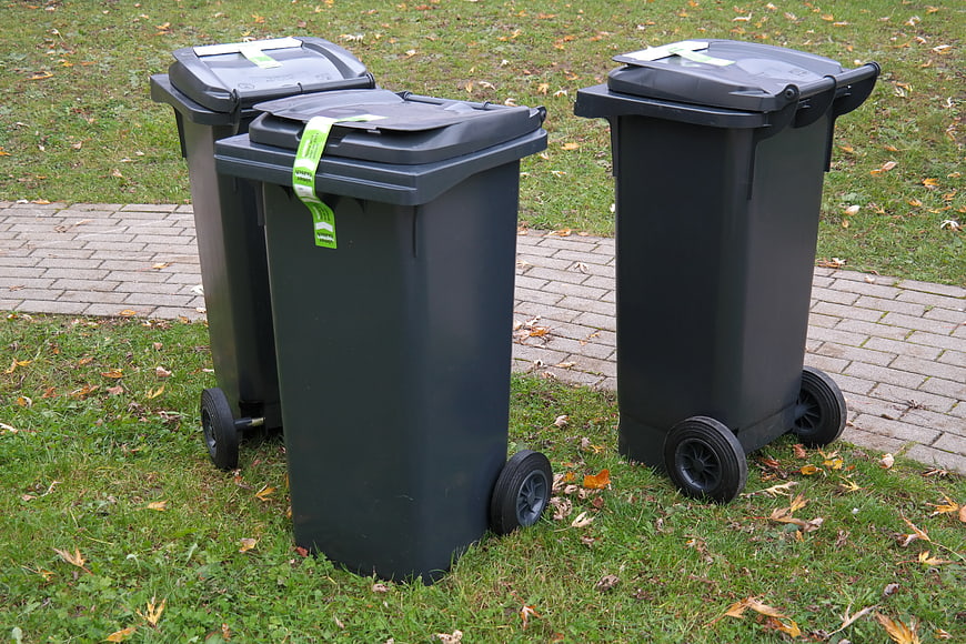 Three black wheeled waste bins on grass with green recycling tags