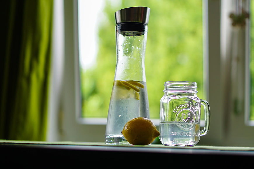 Lemon water in glass carafe and mason jar on windowsill