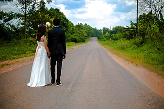 Wedding couple holding hands walking down a rural road