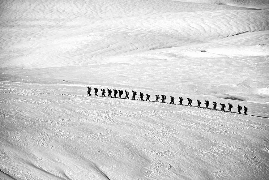 Black and white photo of mountaineers trekking across a vast snowy glacier