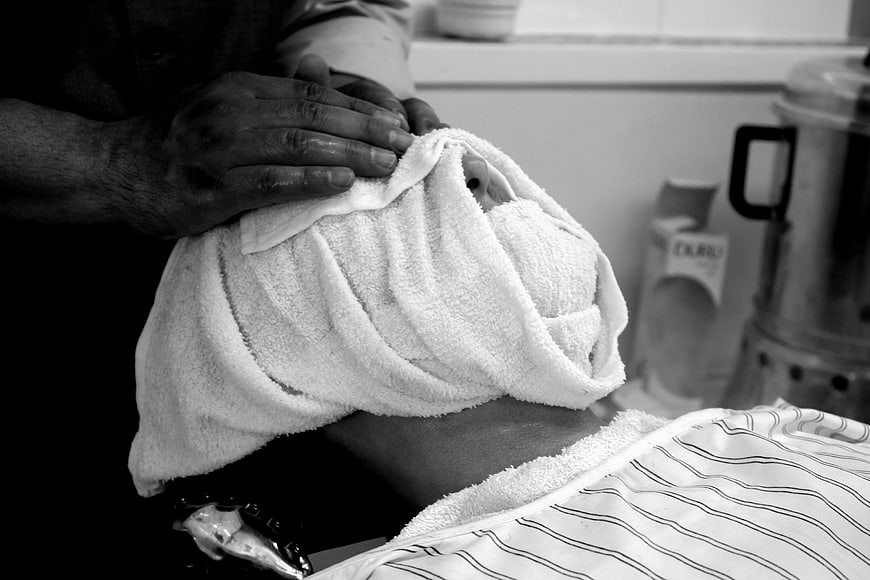 Barber Applying Hot Towel To Client's Head In Black And White