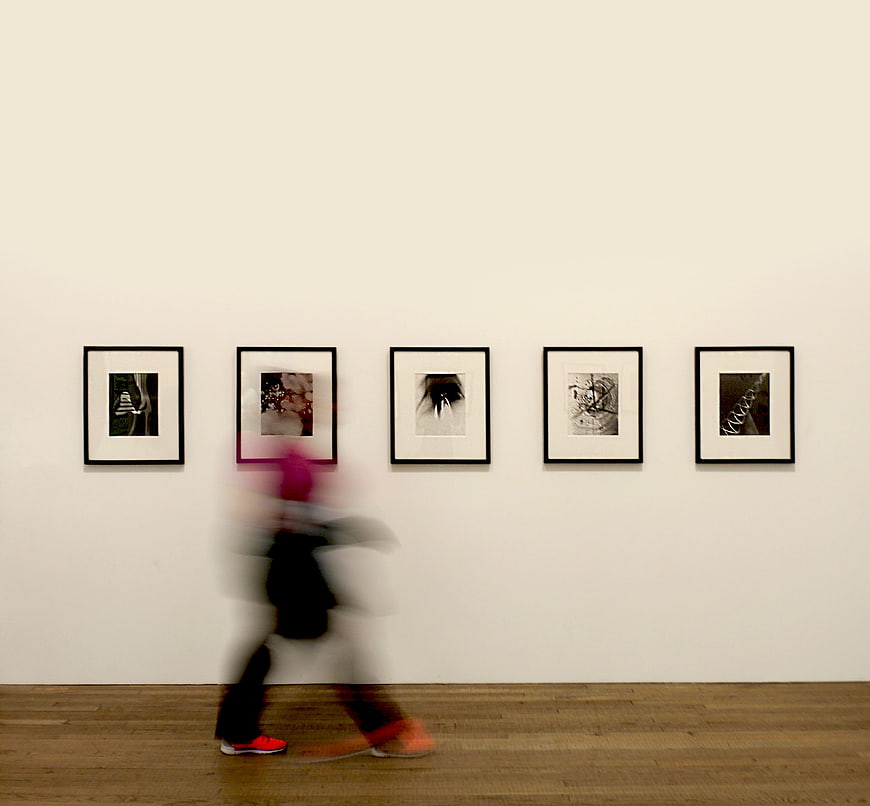Blurred figure walking past framed art in gallery