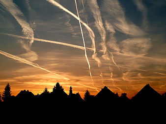 Dramatic sunset sky with airplane contrails over silhouetted rooftops