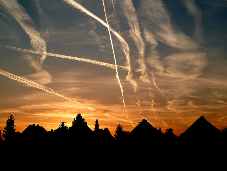 Dramatic sunset sky with airplane contrails over silhouetted rooftops