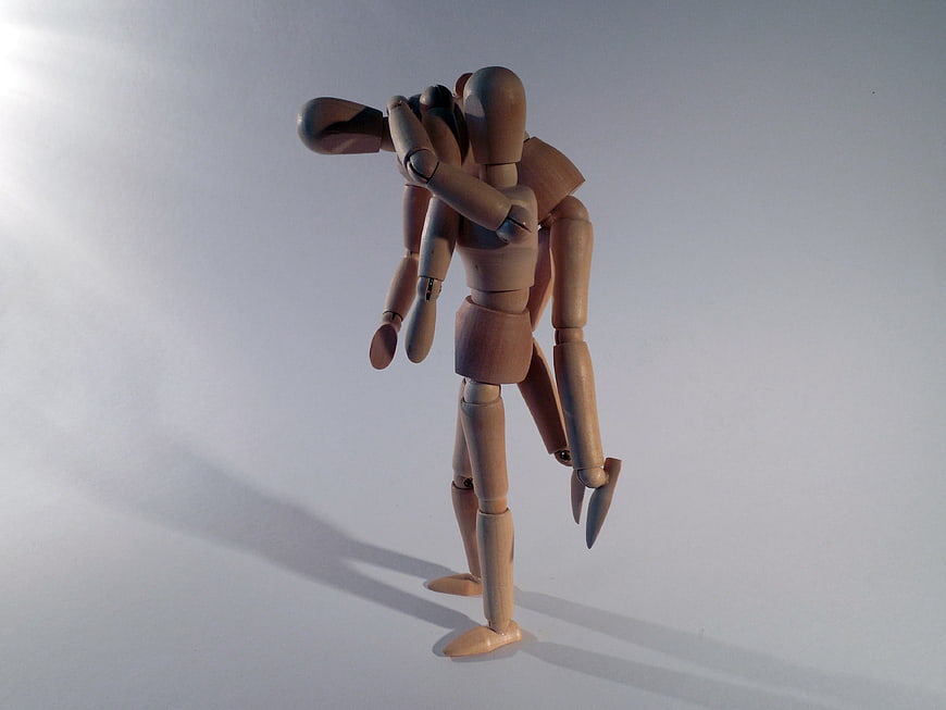 Wooden artist mannequins embracing in a tender hug on a white background