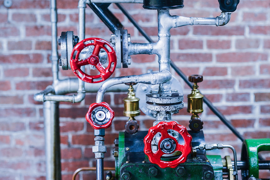 Industrial Pipes and Red Valves on Brick Wall