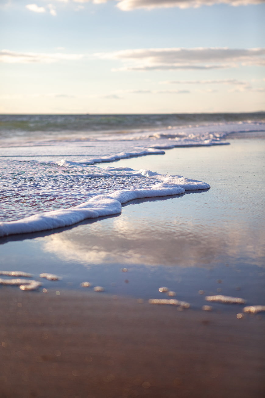 Gentle Ocean Waves Washing Over Wet Sandy Beach at Sunset