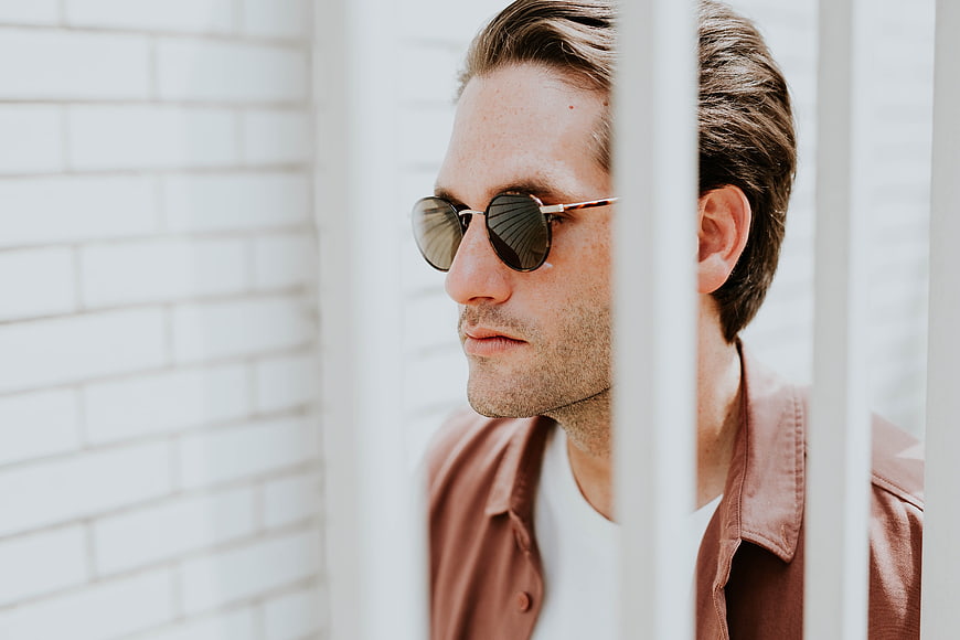 Stylish man in sunglasses looking through white fence